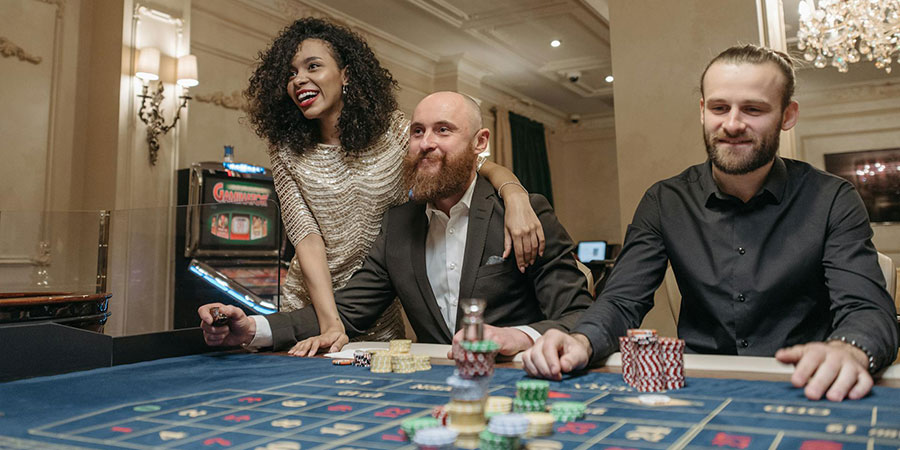 two men in suits and a woman in evening dress playing roulette with plenty of casino chips on a table